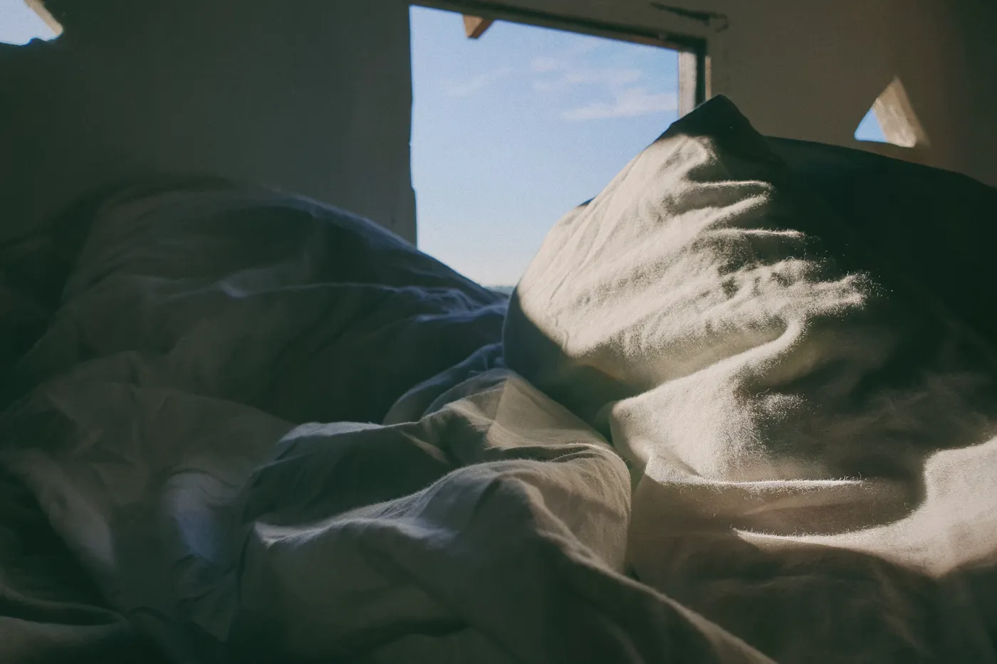 Soft morning sunlight falling across a bed with pale linen