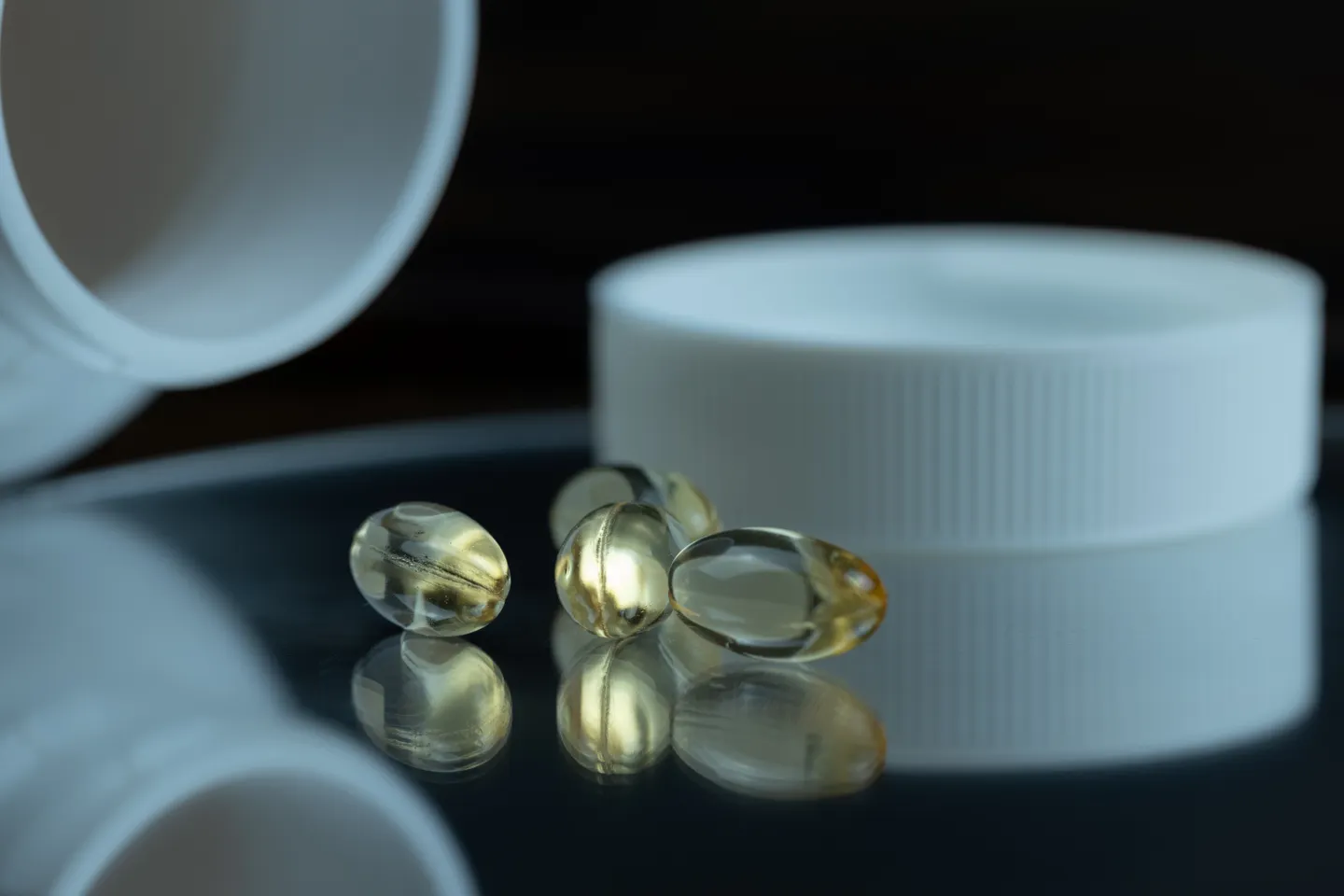 Golden supplement softgel capsules beside an open white bottle and cap