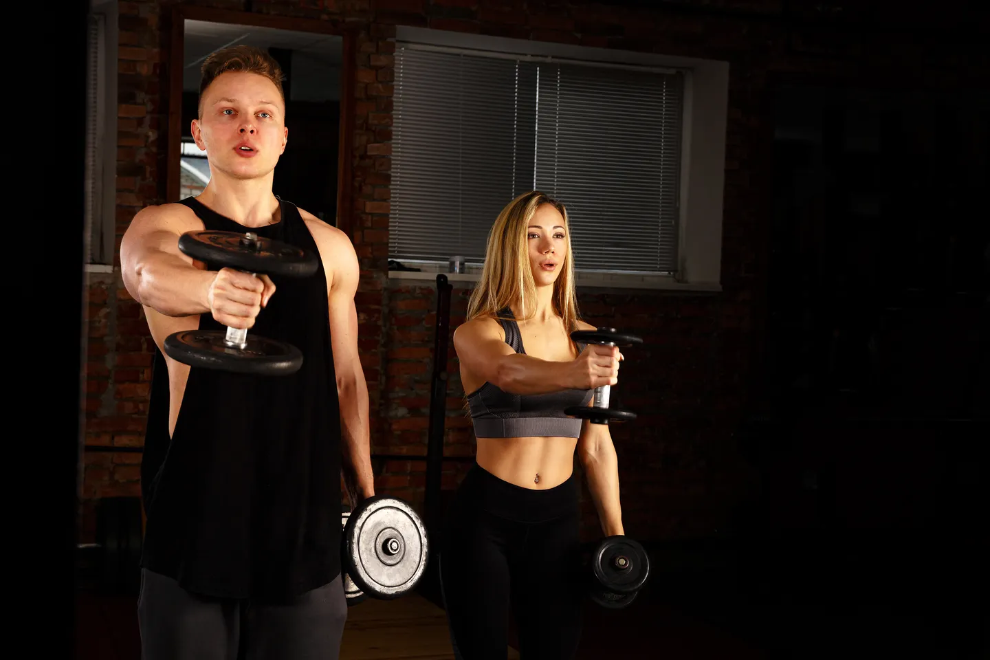 Two adults exercising with dumbbells in a gym